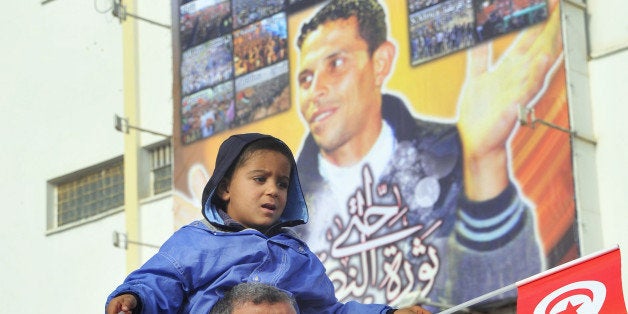 A girl sits high on the shoulders of a grown-up as demonstrators gather to protest against the visit of Tunisian President Moncef Marzouki, Monday, Dec. 17, 2012, in Sidi Bouzid, south Tunisia, the birthplace of the country's recent revolution. Marzouki arrived to mark the revolution's second anniversary. Portrait behind shows Mohammed Bouazizi who set himself on fire in front of the Sidi Bouzid town hall two years ago, after he was publicly slapped and humiliated by a policewoman reprimanding him for selling his vegetables without a license, and died soon afterward, the act which is credited as the catalyst for the Tunisian revolution. (AP Photo/Hichem Borni)