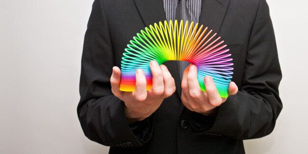 Young man wearing business suit holding colourful slinky between his hands.