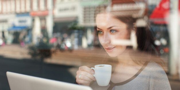 Woman with coffee and laptop looking through window