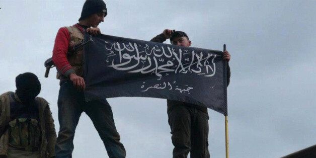 FILE - In this Friday, Jan. 11, 2013 file citizen journalism image provided by Edlib News Network, ENN, which has been authenticated based on its contents and other AP reporting, rebels from al-Qaida-affiliated Jabhat al-Nusra, also known as the Nusra Front, wave their brigade flag, as they step on the top of a Syrian air force helicopter at Taftanaz air base that was captured by the rebels in Idlib province, northern Syria. In the early dawn of Nov. 2, militant leaders with the Islamic State group and al-Qaida gathered at a farm house in northern Syria and sealed a deal to stop fighting each other and work together against their opponents, a prominent Syrian opposition official and a rebel commander said. Such an alliance could be a significant blow to struggling U.S-backed Syrian rebels. (AP Photo/Edlib News Network ENN, File)