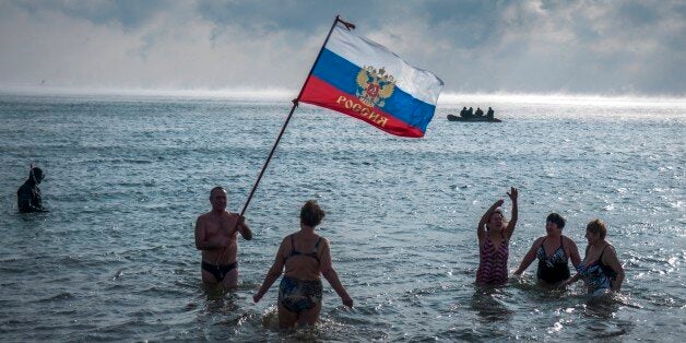 Crimean people wave a Russian national flag as they prepare to swim celebrating an Orthodox Christamas in the Black Sea with air temperature about - 8 Celsius, (17.6 32 Fahrenheit) in Yevpatoria, Crimea, Wednesday, Jan. 7, 2015. Orthodox Christians celebrate Christmas on Jan. 7, in accordance with the Julian calendar. A rescue boat patrols is in the background (AP Photo/Alexander Polegenko)