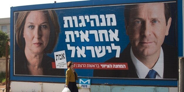 An Israeli woman passes by a campaign poster showing Israeli MP Tzipi Livni (L) and Isaac Herzog co- leaders of the Zionist U