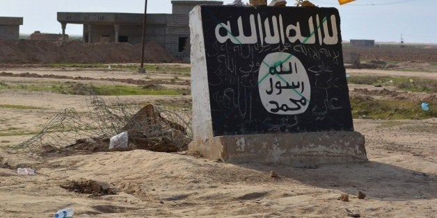 A flag of the Shiite Hezbollah militant group flutters over a mural depicting the emblem of the Islamic State (IS) group in A