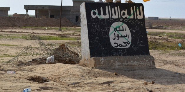 A flag of the Shiite Hezbollah militant group flutters over a mural depicting the emblem of the Islamic State (IS) group in Al-Alam village, northeast of the multi-ethnic Iraqi city of Tikrit, on March 9, 2015, during a military operation by Iraqi government forces and tribal fighters to regain control of the Tikrit region from jihadists. After being forced out of the province of Diyala earlier this year, the IS jihadists are now fighting off a huge assault on the city of Tikrit as government and allied forces continue to work their way north towards the main IS stronghold of Mosul. AFP PHOTO / YOUNIS AL-BAYATI (Photo credit should read YOUNIS AL-BAYATI/AFP/Getty Images)