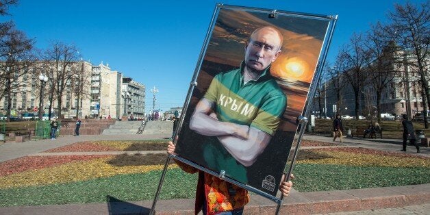 A man carries a picture depicting Russia's President Vladimir Putin in a T-shirt with an inscription reading: 'Crimea' at an open-air political cartoons exhibition dedicated to the one-year anniversary of Crimea voting to leave Ukraine and join the Russian state in central Moscow on March 16, 2015. AFP PHOTO / DMITRY SEREBRYAKOV (Photo credit should read DMITRY SEREBRYAKOV/AFP/Getty Images)