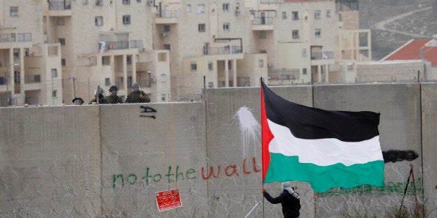 A protestor waves a Palestinian flag in front of Israeli troops during a protest against Israel's separation barrier in the West Bank village of Bilin, near Ramallah, Friday, Feb. 17, 2012. Friday's demonstration marked the 7th anniversary of Palestinians resistance against the barrier at the site. Seen in the back are buildings in the Jewish settlement of Modiin Illit. (AP Photo/Majdi Mohammed)