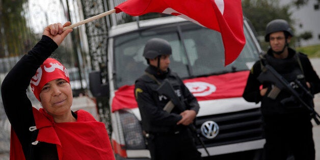 A woman waves the Tunisian flag as policemen stand guard at the National Bardo Museum two days after gunmen attacked the muse