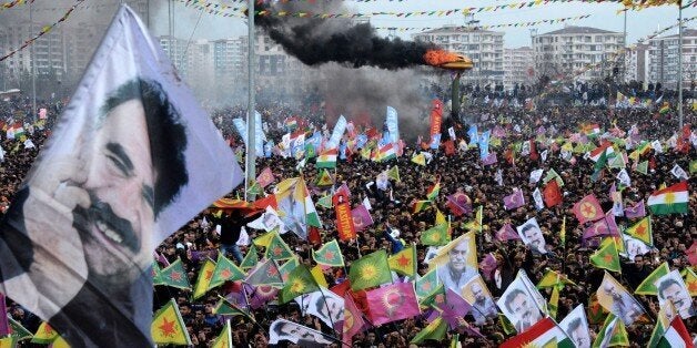 Smoke rises from a fire burning as people wave Kurdish flags and pictures of jailed Kurdish rebel leader Abdullah Ocalan as t