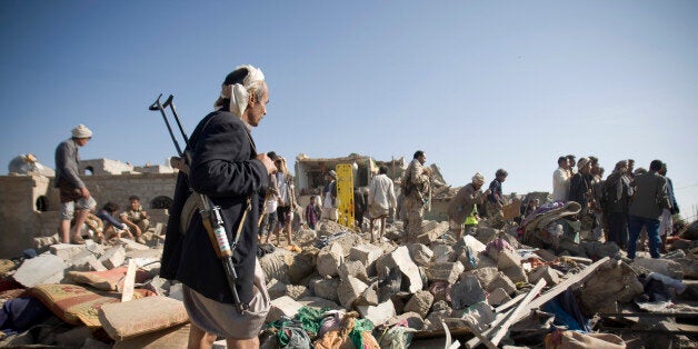 A Houthi Shiite fighter stand guard as people search for survivors under the rubble of houses destroyed by Saudi airstrikes near Sanaa Airport, Yemen, Thursday, March 26, 2015. Saudi Arabia launched airstrikes Thursday targeting military installations in Yemen held by Shiite rebels who were taking over a key port city in the country's south and had driven the embattled president to flee by sea, security officials said. (AP Photo/Hani Mohammed)