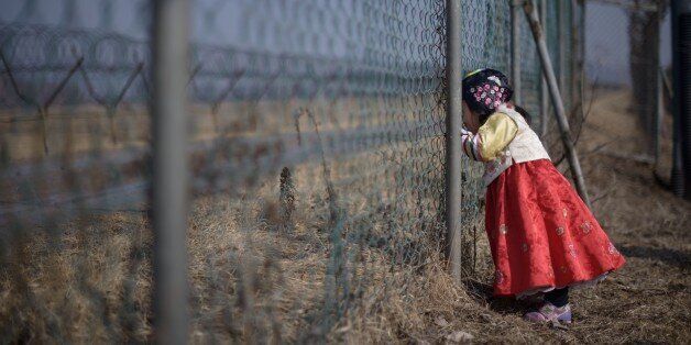A girl wearing a traditional hanbok dress stands at a military fence facing towards North Korea at Imjingak park, south of the Military Demarcation Line and Demilitarized Zone (DMZ) separating North and South Korea, on February 19, 2015. South Korean families separated during the Korean war often visit the DMZ to offer prayers to their relatives in the North, on the occasion of the Lunar New Year. AFP PHOTO / Ed Jones (Photo credit should read ED JONES/AFP/Getty Images)