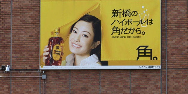 People stand under a huge whisky advertisement of Suntory Holdings Ltd., a Japanese beverage company, in front of Shimbashi Station in Tokyo Tuesday, Jan. 14, 2013. The maker of classic American whiskeys Jim Beam and Maker's Mark has agreed to be acquired by Suntory in a $13.62 billion deal that would create the third largest global premium spirits business. (AP Photo/Koji Sasahara)