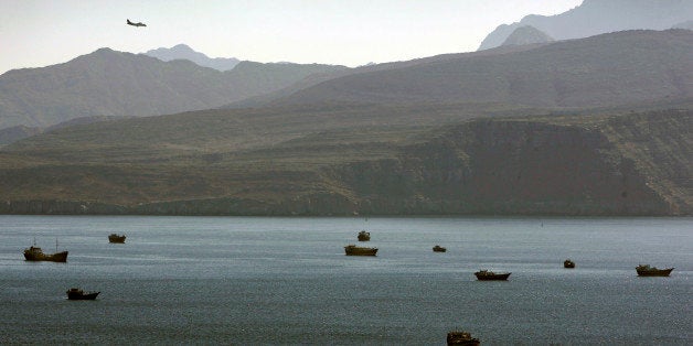 In this Jan. 19, 2012 photo, a plane flies over the mountains in south of the Strait of Hormuz as the trading dhows and ships are docked on the Persian Gulf waters near the town of Khasab, in Oman. Even as sanctions squeeze Iran ever tighter, there's one clandestine route that remains open for business: A short sea corridor connecting a rocky nub of Oman with the Iranian coast about 35 miles (60 kilometers) across the Gulf.(AP Photo/Kamran Jebreili)