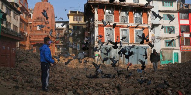 A Nepalese man feeds pigeons as other walkd across the rubble in Kathmandu, Nepal, Friday, May 1, 2015. A strong magnitude earthquake shook Nepal on Saturday devastating the region and leaving some thousands shell-shocked and displaced. (AP Photo/Manish Swarup)