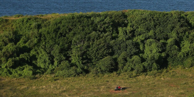 HELGOLAND, GERMANY - AUGUST 04: A couple sits on a bench in grass that covers a crater created by a 5-ton bomb, the largest non-nuclear explosive used in World War II and detonated by the British Royal Air Force, that marks the southern tip on August 4, 2013 on Heligoland Island, Germany. Heligoland Island, in German called Helgoland, lies in the North Sea and until World War II was a popular tourist destination. During the war it became strategically vital and all overground structures were obliterated by massive Allied bombing. Today the island has a population of about 1,200 and is again a popular tourist destination known for its abundant wildlife. (Photo by Sean Gallup/Getty Images)