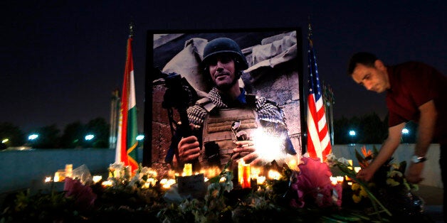 A man lays flowers next to a photograph of James Foley, the freelance journalist killed by the IS group, during a memorial service in Irbil, 350 kilometers (220 miles) north of Baghdad, Iraq, Sunday, Aug.t 24, 2014. Foley, the U.S. journalist slain by Islamic State militants after being held in captivity for nearly two years, was remembered in a small ceremony in Irbil on Sunday. (AP Photo/ Marko Drobnjakovic)