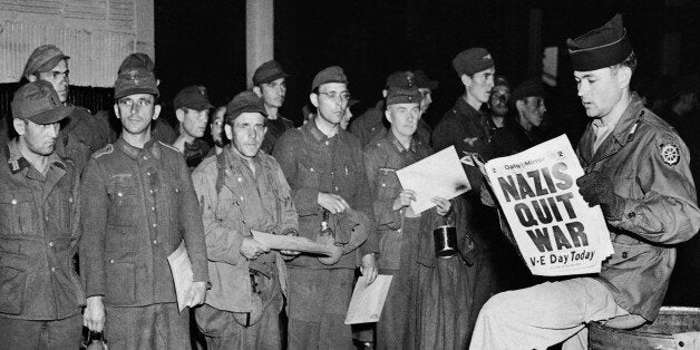 Pfc. Clarence K. Ayers of Evansville, Ind., reads the news of V-E Day as newly arrived German prisoners stand of a New York City pier, May 8, 1945. (AP Photo/John Rooney)