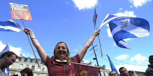 A demonstrator wearing a tartan dress waves Saltire flags, the national flag of Scotland, during a pro-independence rally in
