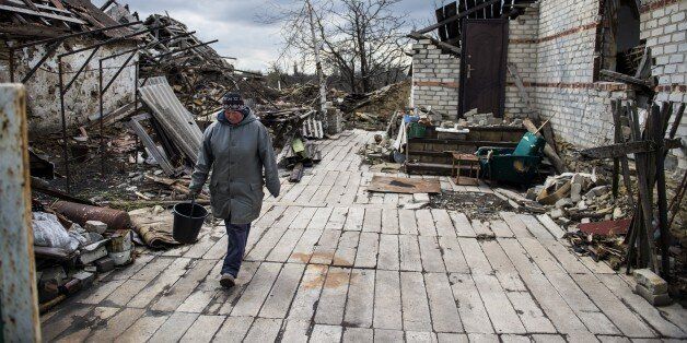 A woman leaves her home which was destroyed to fetch water in the village of Nikishino on April 21, 2015 in the self-proclaimed Donetsk People's Republic (DNR). Only a handful stayed during the fighting here and as people returned to the village counting some 450 houses they found some 240 of those reduced to rubble or had been destroyed beyond repair. The lack of building material and limited emergency food deliveries see mostly elderly people with no were to flee returning and sheltering in their still habitable outhouses. AFP PHOTO / ODD ANDERSEN (Photo credit should read ODD ANDERSEN/AFP/Getty Images)