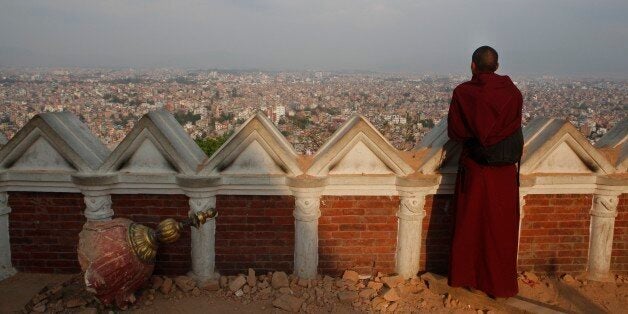 A Buddhist monk catches an aerial view of Kathmandu from the damaged Swayambhunath Stupa premises in Kathmandu, Nepal, Wednes
