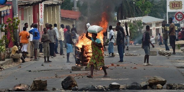 A woman walks past a burning barricade, erected by protestors opposed to the Burundian President's third term, in the Kinanir