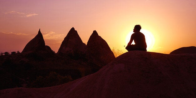 A guy doing some minutes of meditation in front of the beautiful scenery of the Rose Valley close to Cavusin and Goreme in Ca