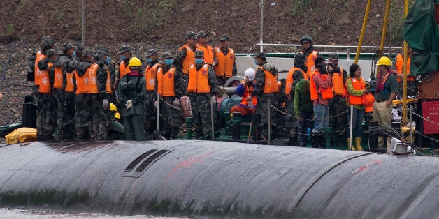 Chinese soldiers stand near a wrapped body as rescuers work on the capsized ship, center, on the Yangtze River in central Chi