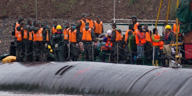 Chinese soldiers stand near a wrapped body as rescuers work on the capsized ship, center, on the Yangtze River in central China's Hubei province Wednesday, June 3, 2015. Hopes dimmed Wednesday for rescuing more than 400 people still trapped in the capsized river cruise ship that overturned in stormy weather, as hundreds of rescuers searched the Yangtze River site in what could become the deadliest Chinese maritime accident in decades. (AP Photo/Andy Wong)