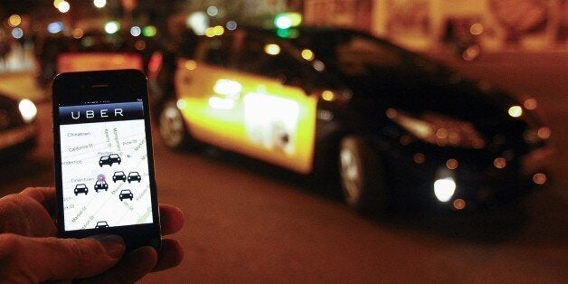 The Uber app is seen on a smartphone past cabs waiting for clients near the Sagrada Familia in Barcelona, on December 9, 2014