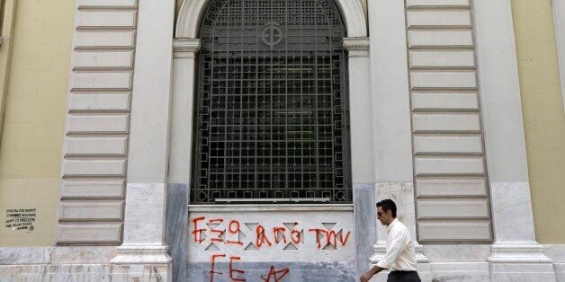 A pedestrian passes a sign reads ''Out of EU (European Union)'' at the headquarters of National Bank of Greece in Athens, Wed