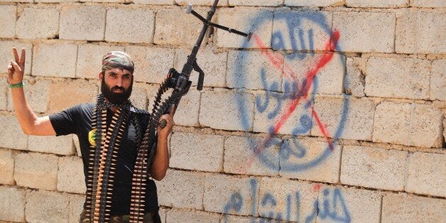 A heavily armed Iraqi Shiite fighter from the Popular Mobilisation units flashes the V for victory sign in front of graffiti of the Islamic State (IS) group in the town of Baiji, north of Tikrit, as allied Iraqi forces fight against the jihadist group to try to retake the strategic town for a second time, on June 9, 2015. Baghdad regained control of Baiji -- located on the road to IS hub Mosul and near the country's largest oil refinery -- last year, but subsequently lost it again. AFP PHOTO/AHMAD AL-RUBAYE (Photo credit should read AHMAD AL-RUBAYE/AFP/Getty Images)