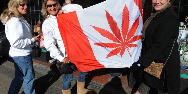 Visitors pose in front of a flag similiar to the Canadian one but showing a cannabis plant instead of a maple leaf at a store in Eastside Vancouver during the Vancouver Winter Olympics on February 22, 2010. AFP PHOTO/Mark RALSTON (Photo credit should read MARK RALSTON/AFP/Getty Images)