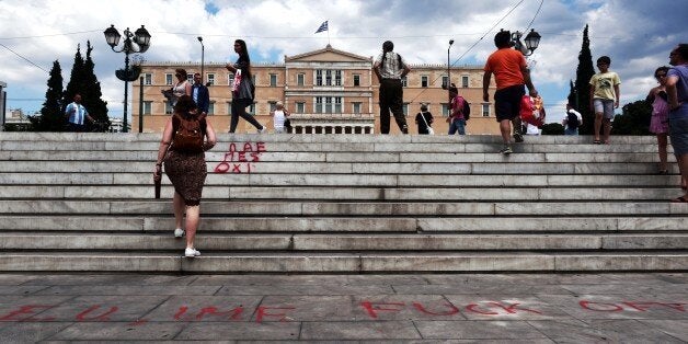 People walk past an anti EU (European Union) and anti IMF (International Monetary Fund) slogan in front of the Greek parliame