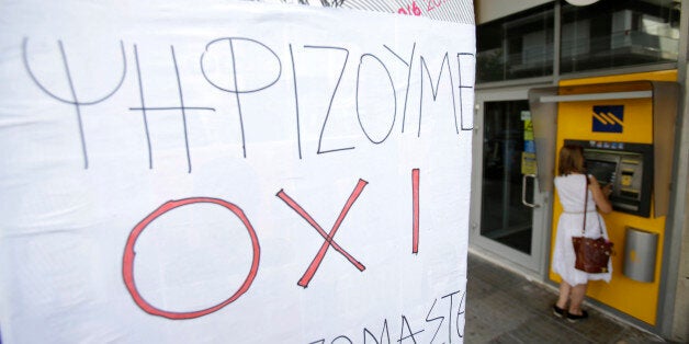 A woman uses an ATM of a closed bank as a sign that reads: ''We vote NO'' referring to the upcoming referendum, in Athens, Monday, June 29, 2015. Greece's five-year financial crisis took its most dramatic turn yet, with the cabinet deciding that Greek banks would remain shut for six business days and restrictions would be imposed on cash withdrawals. (AP Photo/Thanassis Stavrakis)