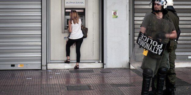 A woman withdraws money from an ATM, as police stand guard in Athens on July 2, 2015, during a demonstration supporting the no vote for the upcoming referendum. Greece's government and international creditors raised the stakes on July 2 over a weekend referendum seen as decisive for the nearly insolvent EU country's political and financial future. While Prime Minister Alexis Tsipras has urged Greeks to vote 'No' to the austerity measures demanded by international creditors, opposition parties including the centre-right New Democracy are campaigning for a 'Yes' vote in the referendum on July 5. AFP PHOTO / Louisa Gouliamaki (Photo credit should read LOUISA GOULIAMAKI/AFP/Getty Images)