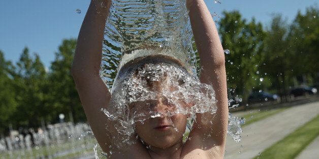 BERLIN, GERMANY - JULY 01: Paul, 9, dumps a bucket of water over his head at a fountain near government buildings during hot weather on July 1, 2015 in Berlin, Germany. Temperatures across northern Europe are rising and in Germany a high of 36 degrees is forecast for the weekend. (Photo by Sean Gallup/Getty Images)