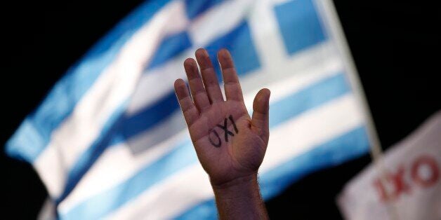 A demonstrator rises his hand reading the word ''No'' as a Greek flag waves during a rally organized by supporters of the No vote in Athens, Friday, July 3, 2015. A new opinion poll shows a dead heat in Greece's referendum campaign with just two days to go before Sunday's vote on whether Greeks should accept more austerity in return for bailout loans. (AP Photo/Petros Giannakouris)