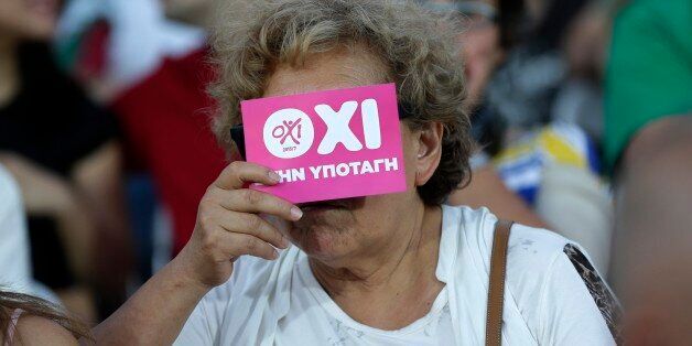 A supporter of the No vote covers her face with a flyer reading ''No to submission'' at Klafthmonos square in Athens, Sunday, July 5, 2015. Greece faced an uncharted future as its interior ministry predicted Sunday that more than 60 percent of voters in a hastily called referendum had rejected creditors' demands for more austerity in exchange for rescue loans.(AP Photo/Petr David Josek)