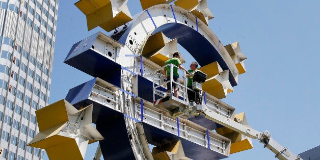 Two workers stand on a lifting platform during renovation works at the Euro sculpture in front of the old European Central Bank in Frankfurt, Germany, Monday, July 6, 2015. The sculpture will be renovated during the next four days. (AP Photo/Michael Probst)