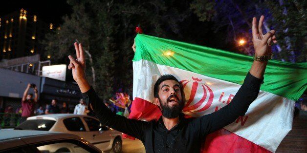 An Iranian man flashes the victory sign as an other holds the Iranian national flag during celebration in northern Tehran on July 14, 2015,after Iran's nuclear negotiating team struck a deal with world powers in Vienna. Major powers clinched a historic deal Tuesday aimed at ensuring Iran does not obtain the nuclear bomb, opening up Tehran's stricken economy and potentially ending decades of bad blood with the West.AFP PHOTO/ATTA KENARE (Photo credit should read ATTA KENARE/AFP/Getty Images)