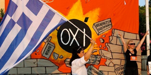 A demonstrator makes the victory sign in front of a banner, depicting a medal ball reading ''NO'' and destroying a wall with anti-austerity measures as another one waves a Greek flag during a rally in Athens, Friday, June 10, 2015. Greek Prime Minister Alexis Tsipras sought his left-wing party's backing on Friday for a new budget austerity package that is harsher than what he urged Greeks to reject in a vote just last week, but would provide the country will longer-term financial support. (AP Photo/Petros Karadjias)