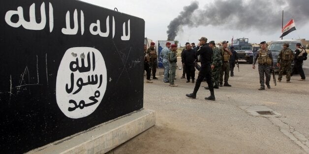 Iraqi security forces and Shiite fighters from the Popular Mobilisation units gather next to a mural depicting the emblem of the Islamic State (IS) group outside one of the presidential palaces in Tikrit, on April 1, 2015, a day after the prime minister declared victory in the weeks-long battle to retake the city from the IS group. Iraqi forces battled the last jihadists the northern city on April 1, 2015 to seal a victory the government described as a milestone in efforts to rid the country of the Islamic State group. AFP PHOTO / AHMAD AL-RUBAYE (Photo credit should read AHMAD AL-RUBAYE/AFP/Getty Images)