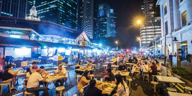 Diners sit at restaurant tables at the Lau Pa Sat food court as commercial buildings stand illuminated at night in the central business district city of Singapore, on Sunday, March 22, 2015. Lee Kuan Yew, who helped transform Singapore from a colonial trading center into one of Asia's most prosperous nations during 31 years as its first elected prime minister, has died. He was 91. Photographer: Nicky Loh/Bloomberg via Getty Images