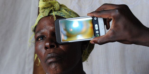 TO GO WITH AFP STORY BY IRENE WAIRIMU This photo taken on August 28, 2013, in Kianjokoma village, near Kenya's lakeside town of Naivasha, shows a technician scanning the eye of a woman with a smartphone application as she takes part in an ophthalmological study and examination, carried out by technicians from the 'Nakuru Eye Disease Cohort Study', led by Dr. Andrew Bastawrous (unseen) of the London School of Hygiene and Tropical Medicine, in which a smartphone application is used to scan people's eyes and optic nerves, to detect eye diseases, including cataracts and glaucoma. The 'Eyephone app', a smartphone application which can detect eye diseases and disorders, could potentially provide low-income and poor Kenyans with an opportunity to get a quick and effective diagnosis of their eye problems, even in remote rural areas. The equipment used in the study, which has been running for five years and is now in its final stages, is a smartphone with add-on lens that scans the retina, plus an application to record the data. The technology is deceptively simple to use and extremely cheap: each 'Eye-Phone', costs a few hundred euros (dollars), compared to a professional ophthalmoscope that costs tens of thousands of euros and weighs in at around 130 kilogrammes (290 pounds). Dr. Andrew Bastawrous of the London School of Hygiene and Tropical Medicine, who has led the study surrounding the 'Eye-Phone', hopes the 'Nakuru Eye Disease Cohort Study', which has done the rounds of 5,000 Kenyan patients, will one day revolutionalise access to eye treatment for millions of low income Africans who are suffering from eye disease and blindness. AFP PHOTO / TONY KARUMBA (Photo credit should read TONY KARUMBA/AFP/Getty Images)