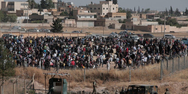 In this photo taken from the Turkish side of the border between Turkey and Syria, in Akcakale, Sanliurfa province, southeastern Turkey, Turkish army, bottom, watch as Syrian refugees wait on the Syrian side of the border in order to cross, Saturday, June 13, 2015. Turkey's emergency management agency says more than 6,000 Syrians have crossed into Turkey in the past week, fleeing fighting between Islamic State militants and Kurdish forces near the northern Syrian city of Tel Abyad. (AP Photo/Lefteris Pitarakis)