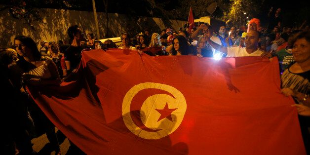 People carry a Tunisian flag during an protest against terrorism in Sousse, Tunisia, Saturday, June 27, 2015. Tunisia's postcard destination for tourists is reeling from the terror that blighted another day of play at the Mediterranean seaside resort of Sousse. A man armed with a Kalashnikov and grenades gunned down tourists on a private beach Friday, and then moved methodically through the grounds of a luxury hotel â to the swimming pool, reception area and offices. (AP Photo/Darko Vojinovic)
