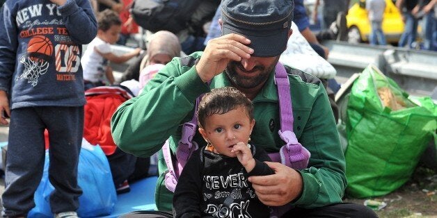 A man holds a baby girl as migrants and refugees sit on the asphalt at the official border crossing between Serbia and Hungar