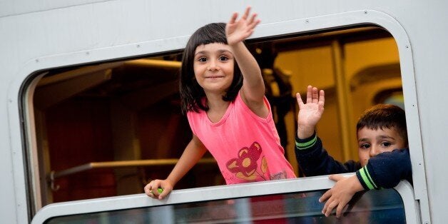 Refugee children wave as they sit in a special train heading to western German town of Dortmund at the main train station in Munich, southern Germany, on September 13, 2015. Thousands of refugees arrived in Germany during the weekend, coming from Hungary and Austria. AFP PHOTO / DPA / SVEN HOPPE +++ GERMANY OUT (Photo credit should read SVEN HOPPE/AFP/Getty Images)