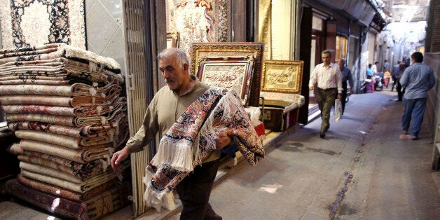 In this Monday, Aug. 10, 2015 photo, an Iranian man carries a carpet through Tehran's old, main bazaar, Iran. Iran's famed ca