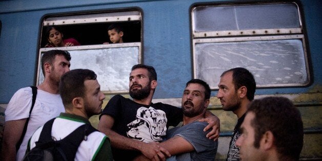 A man carries a disabled man as migrants and refugees queue to board the train heading to Serbia near the town of Gevgelija a