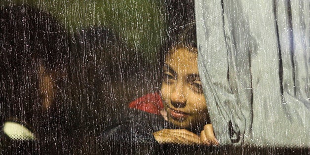 A girl looks out of a window as she sits in a bus which will transport migrants and refugees to a camp, after they were regis
